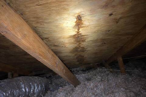 Flashlight beam on the underside of roof decking in an attic, a dark water trail running down from a nail tip