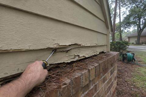Lower edge of hardboard lap siding on a gable, swollen and crumbling above a brick ledge